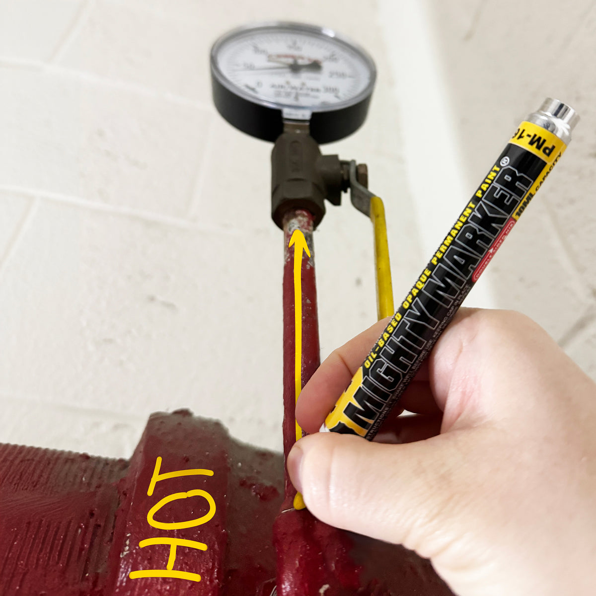 Hand marking a red metal object with a yellow Mighty Marker
