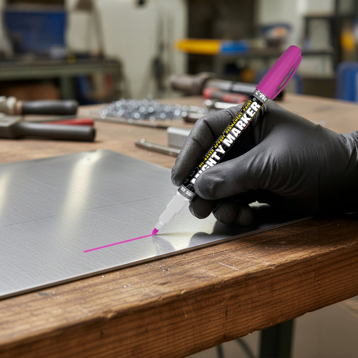 Hand wearing a black glove using a pink pm-24 mighty marker on metal sheet in a workshop setting